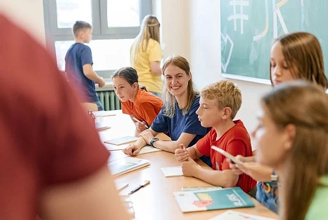 Mehrere Kinder in knalligen farbigen T-Shirts an einem Tisch. Ein Mädchen in der Mitte lacht in die Kamera